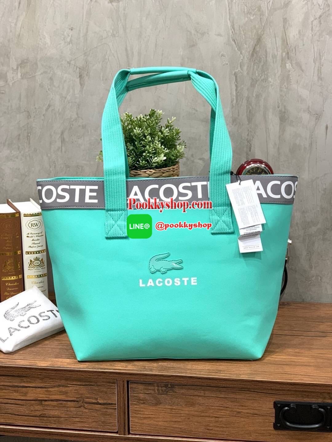 ลาคอส Shopping Bag กระเป๋าถือทรงช้อปปิ้งขนาดใหญ่ ที่ใส่สัมภาระได้รวมถึงใส่เอกสารขนาด A4 ได้ วัสดุ PVC กันน้ำ ดูแลรักษาง่าย ตัดขอบด้วยแถบโลโก้สีเทา ด้านหน้าสกรีนโลโก้และประดับจรเข้อันเป็นสัญลักษณ์ เปิดปิดด้วยซิปเดียว ภายในสกรีนโลโก้แบรนด์ ใบใหญ่สวยโดดเด่