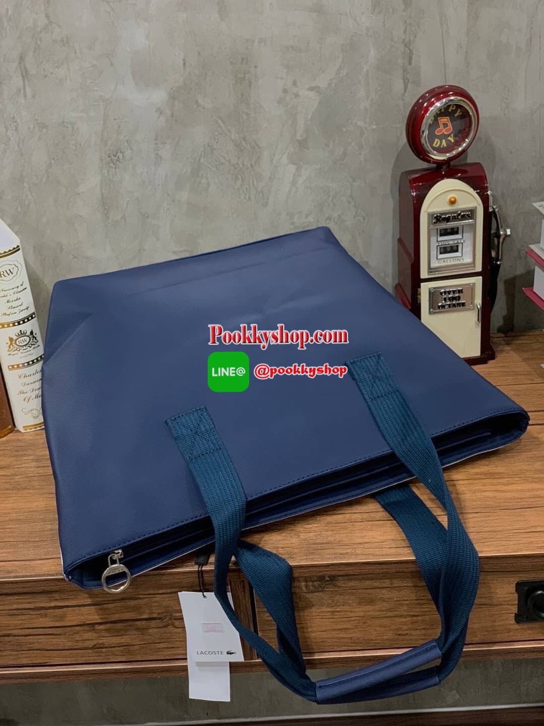 ลาคอส Shopping Bag กระเป๋าถือทรงช้อปปิ้งขนาดใหญ่ ที่ใส่สัมภาระได้รวมถึงใส่เอกสารขนาด A4 ได้ วัสดุ PVC กันน้ำ ดูแลรักษาง่าย ตัดขอบด้วยแถบโลโก้สีเทา ด้านหน้าสกรีนโลโก้และประดับจรเข้อันเป็นสัญลักษณ์ เปิดปิดด้วยซิปเดียว ภายในสกรีนโลโก้แบรนด์ ใบใหญ่สวยโดดเด่