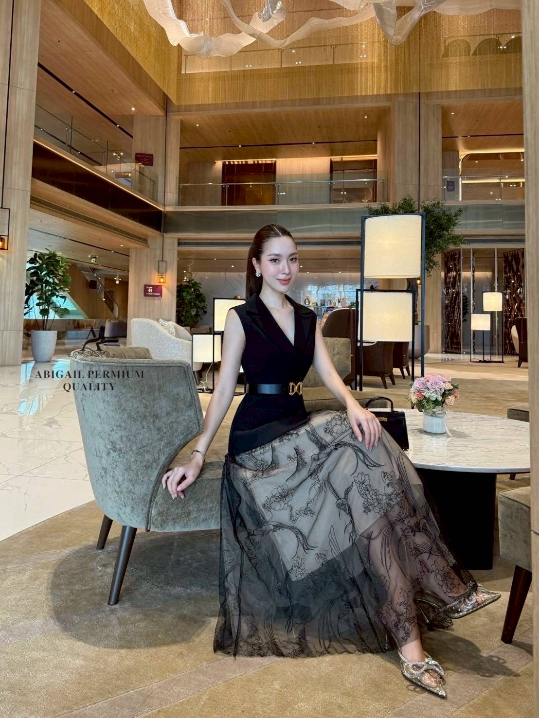 เสื้อแขนกุดเบลเซอร์สีดำ ดีไซน์คอวีลึก เพิ่มความเรียบหรูพร้อมกระดุมด้านหน้าและกระเป๋าดีไซน์เรียบเท่ ดึงความสนใจด้วยเข็มขัดหนังหัวสีทองที่ช่วยเน้นทรวดทรงและเพิ่มความพรีเมียม กระโปรงยาวทรงเอ ผ้าซีทรูสองชั้น ด้านในเป็นผ้าสีเบจเรียบ ส่วนด้านนอกเป็นผ้าทูลล์สีดำ