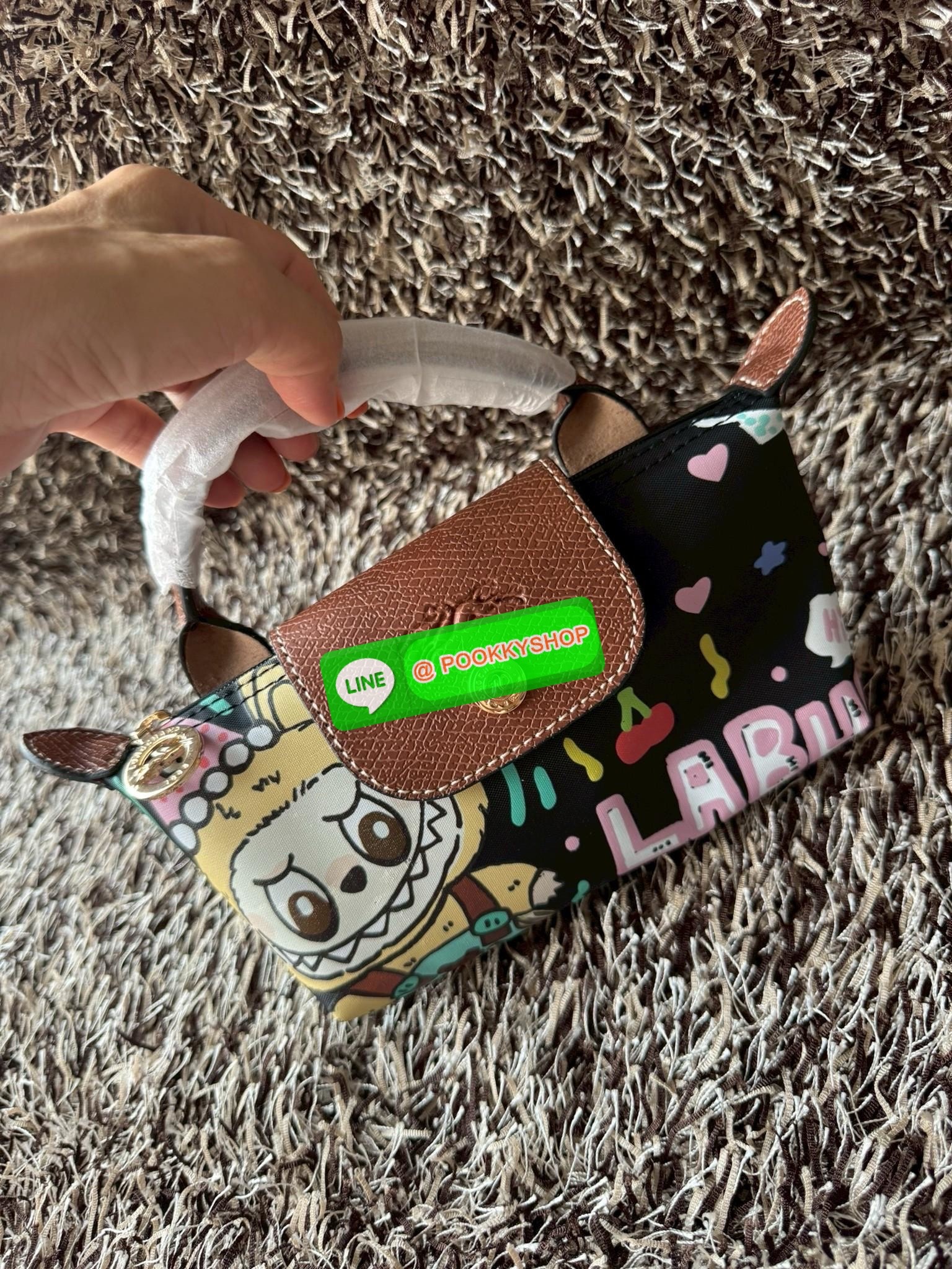 LONGCHAMP LE PLIAGE ORIGINAL X Labubu Pouch with handle เป็นการร่วมงานกัระหว่างแบรนด์ และยังกระเป๋าถือขนาดมินิทรงpouch ที่ด้านหน้ามีลวดลายน้องลาบูบู้ในแบบต่างๆ เปิดปิดระบบสองชั้น ได้ว่าของด้านในมีความปลอดภัย เหมาะอย่างยิ่งสำหรับสาวๆที่ชอบกระเป๋าขนาดมินิไซ