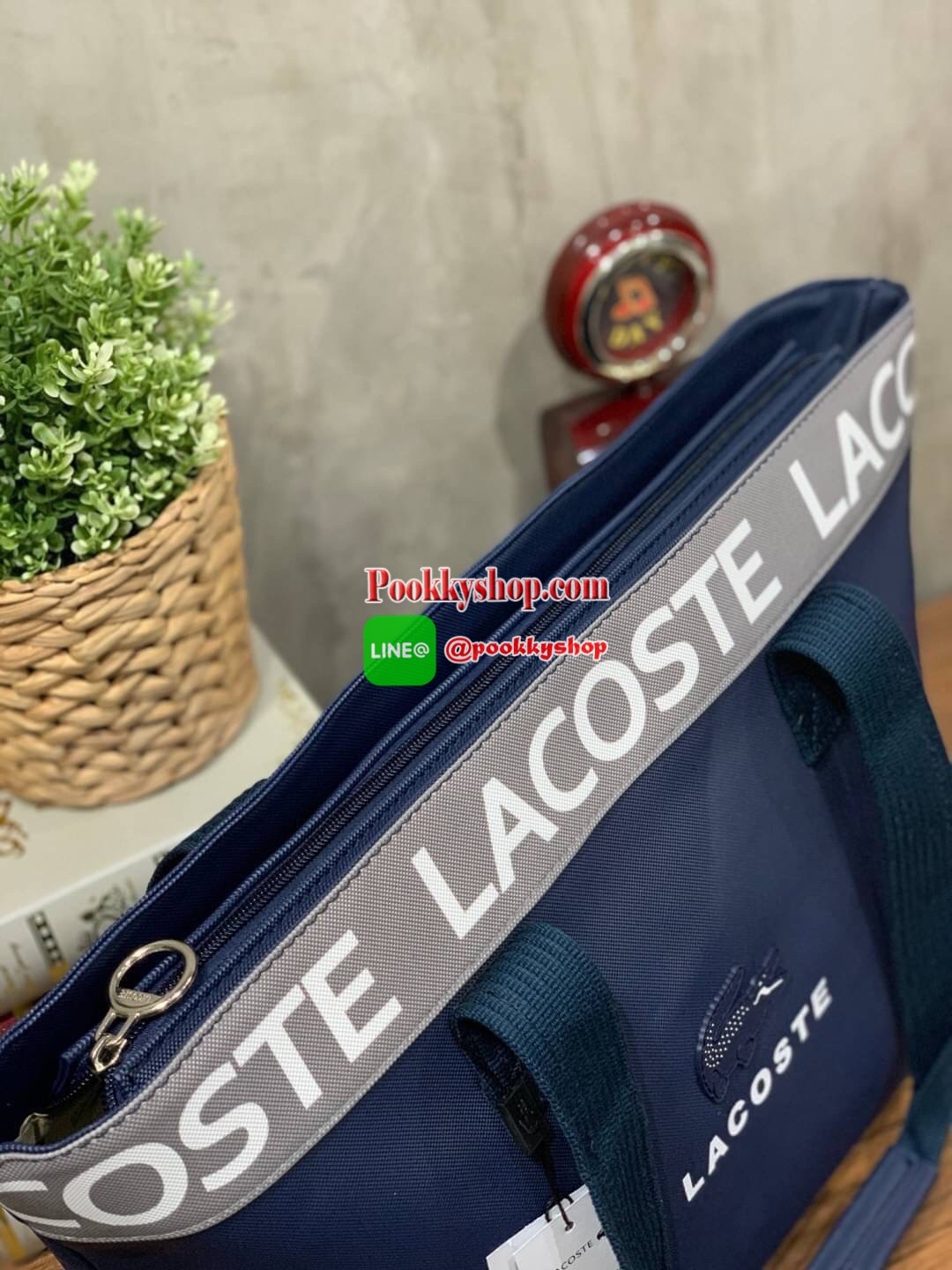 ลาคอส Shopping Bag กระเป๋าถือทรงช้อปปิ้งขนาดใหญ่ ที่ใส่สัมภาระได้รวมถึงใส่เอกสารขนาด A4 ได้ วัสดุ PVC กันน้ำ ดูแลรักษาง่าย ตัดขอบด้วยแถบโลโก้สีเทา ด้านหน้าสกรีนโลโก้และประดับจรเข้อันเป็นสัญลักษณ์ เปิดปิดด้วยซิปเดียว ภายในสกรีนโลโก้แบรนด์ ใบใหญ่สวยโดดเด่