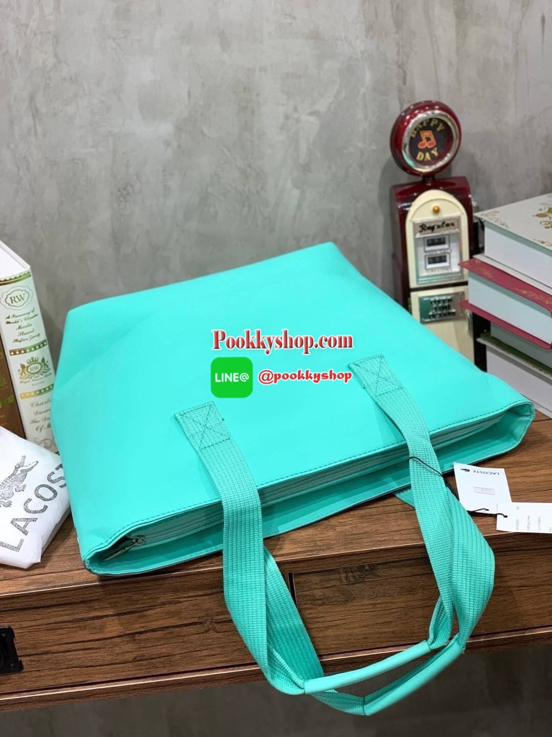 ลาคอส Shopping Bag กระเป๋าถือทรงช้อปปิ้งขนาดใหญ่ ที่ใส่สัมภาระได้รวมถึงใส่เอกสารขนาด A4 ได้ วัสดุ PVC กันน้ำ ดูแลรักษาง่าย ตัดขอบด้วยแถบโลโก้สีเทา ด้านหน้าสกรีนโลโก้และประดับจรเข้อันเป็นสัญลักษณ์ เปิดปิดด้วยซิปเดียว ภายในสกรีนโลโก้แบรนด์ ใบใหญ่สวยโดดเด่