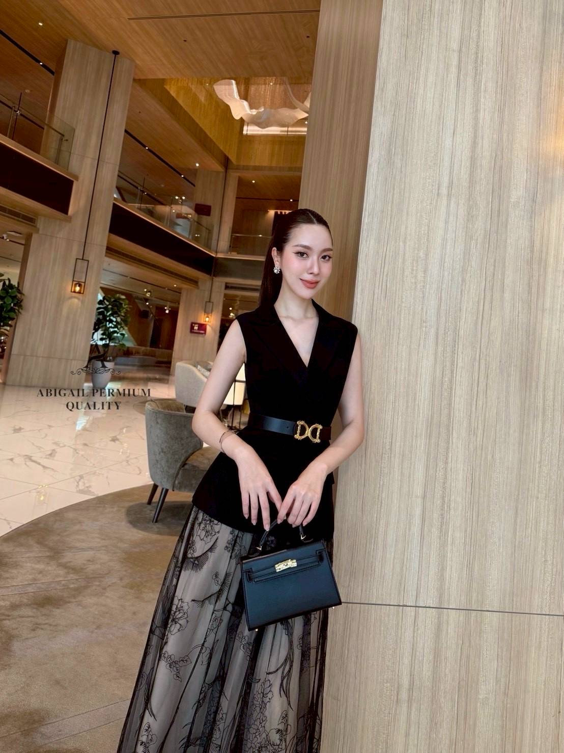 เสื้อแขนกุดเบลเซอร์สีดำ ดีไซน์คอวีลึก เพิ่มความเรียบหรูพร้อมกระดุมด้านหน้าและกระเป๋าดีไซน์เรียบเท่ ดึงความสนใจด้วยเข็มขัดหนังหัวสีทองที่ช่วยเน้นทรวดทรงและเพิ่มความพรีเมียม กระโปรงยาวทรงเอ ผ้าซีทรูสองชั้น ด้านในเป็นผ้าสีเบจเรียบ ส่วนด้านนอกเป็นผ้าทูลล์สีดำ