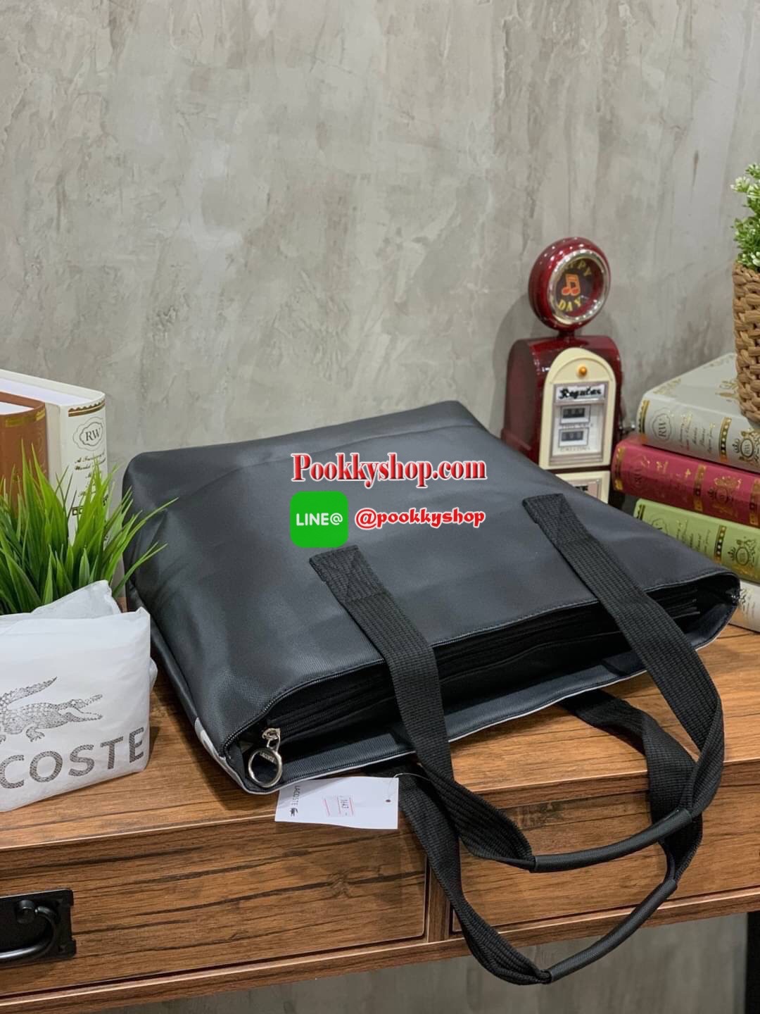 ลาคอส Shopping Bag กระเป๋าถือทรงช้อปปิ้งขนาดใหญ่ ที่ใส่สัมภาระได้รวมถึงใส่เอกสารขนาด A4 ได้ วัสดุ PVC กันน้ำ ดูแลรักษาง่าย ตัดขอบด้วยแถบโลโก้สีเทา ด้านหน้าสกรีนโลโก้และประดับจรเข้อันเป็นสัญลักษณ์ เปิดปิดด้วยซิปเดียว ภายในสกรีนโลโก้แบรนด์ ใบใหญ่สวยโดดเด่