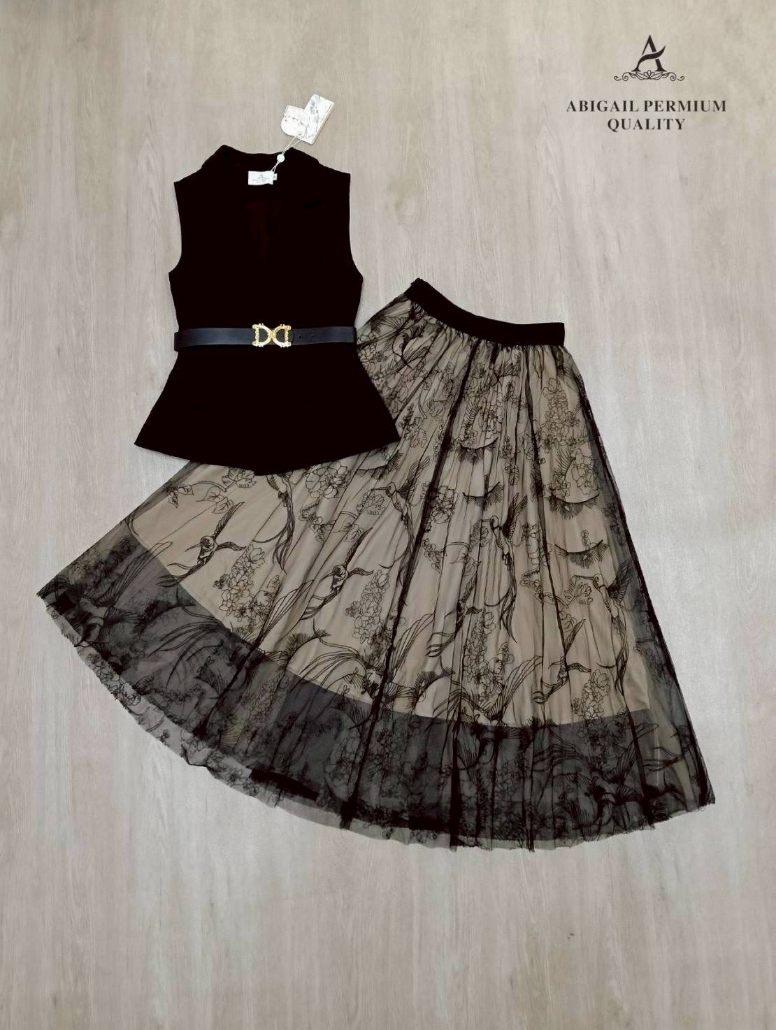 เสื้อแขนกุดเบลเซอร์สีดำ ดีไซน์คอวีลึก เพิ่มความเรียบหรูพร้อมกระดุมด้านหน้าและกระเป๋าดีไซน์เรียบเท่ ดึงความสนใจด้วยเข็มขัดหนังหัวสีทองที่ช่วยเน้นทรวดทรงและเพิ่มความพรีเมียม กระโปรงยาวทรงเอ ผ้าซีทรูสองชั้น ด้านในเป็นผ้าสีเบจเรียบ ส่วนด้านนอกเป็นผ้าทูลล์สีดำ