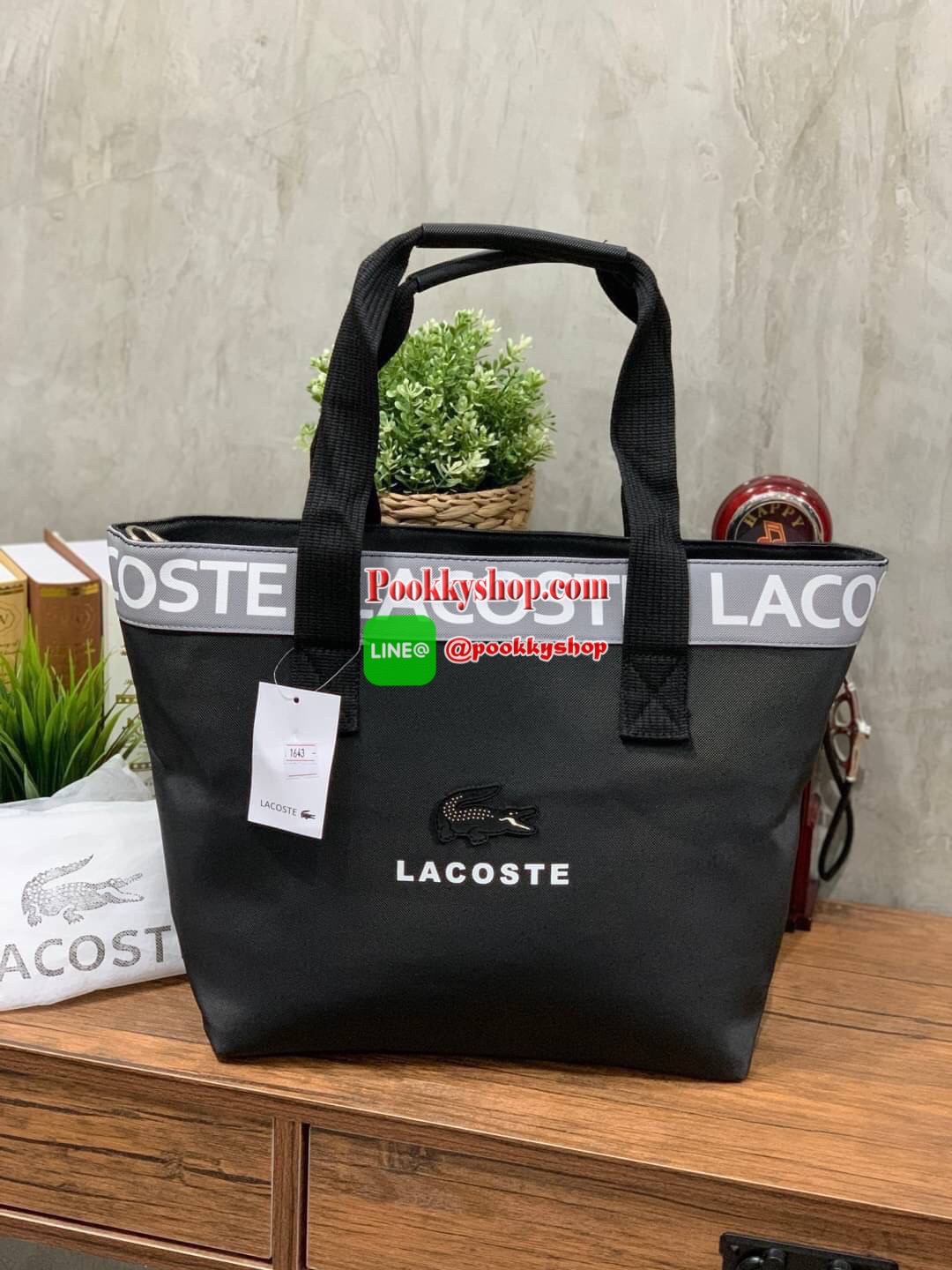 ลาคอส Shopping Bag กระเป๋าถือทรงช้อปปิ้งขนาดใหญ่ ที่ใส่สัมภาระได้รวมถึงใส่เอกสารขนาด A4 ได้ วัสดุ PVC กันน้ำ ดูแลรักษาง่าย ตัดขอบด้วยแถบโลโก้สีเทา ด้านหน้าสกรีนโลโก้และประดับจรเข้อันเป็นสัญลักษณ์ เปิดปิดด้วยซิปเดียว ภายในสกรีนโลโก้แบรนด์ ใบใหญ่สวยโดดเด่