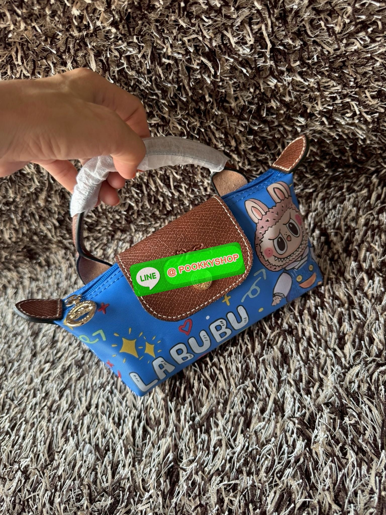 LONGCHAMP LE PLIAGE ORIGINAL X Labubu Pouch with handle เป็นการร่วมงานกัระหว่างแบรนด์ และยังกระเป๋าถือขนาดมินิทรงpouch ที่ด้านหน้ามีลวดลายน้องลาบูบู้ในแบบต่างๆ เปิดปิดระบบสองชั้น ได้ว่าของด้านในมีความปลอดภัย เหมาะอย่างยิ่งสำหรับสาวๆที่ชอบกระเป๋าขนาดมินิไซ