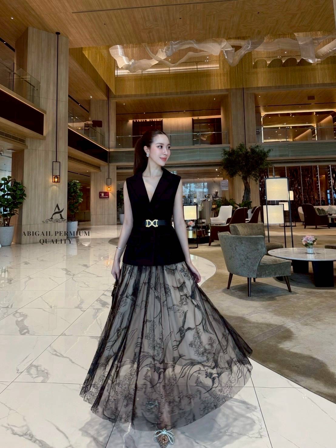 เสื้อแขนกุดเบลเซอร์สีดำ ดีไซน์คอวีลึก เพิ่มความเรียบหรูพร้อมกระดุมด้านหน้าและกระเป๋าดีไซน์เรียบเท่ ดึงความสนใจด้วยเข็มขัดหนังหัวสีทองที่ช่วยเน้นทรวดทรงและเพิ่มความพรีเมียม กระโปรงยาวทรงเอ ผ้าซีทรูสองชั้น ด้านในเป็นผ้าสีเบจเรียบ ส่วนด้านนอกเป็นผ้าทูลล์สีดำ