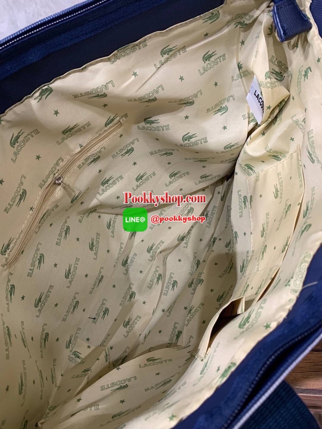 ลาคอส Shopping Bag กระเป๋าถือทรงช้อปปิ้งขนาดใหญ่ ที่ใส่สัมภาระได้รวมถึงใส่เอกสารขนาด A4 ได้ วัสดุ PVC กันน้ำ ดูแลรักษาง่าย ตัดขอบด้วยแถบโลโก้สีเทา ด้านหน้าสกรีนโลโก้และประดับจรเข้อันเป็นสัญลักษณ์ เปิดปิดด้วยซิปเดียว ภายในสกรีนโลโก้แบรนด์ ใบใหญ่สวยโดดเด่